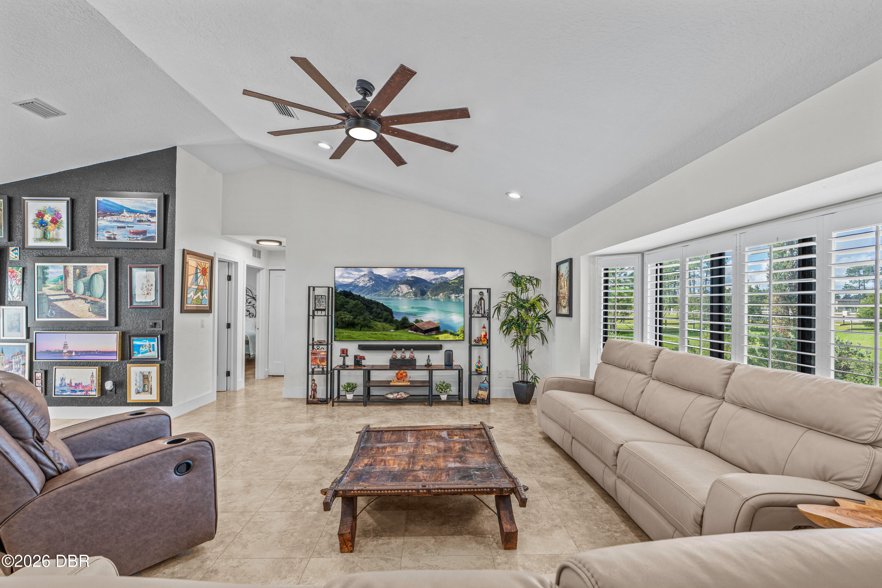 Furnished living room with a beige sectional, leather recliners, rustic coffee table, and wide shuttered windows.