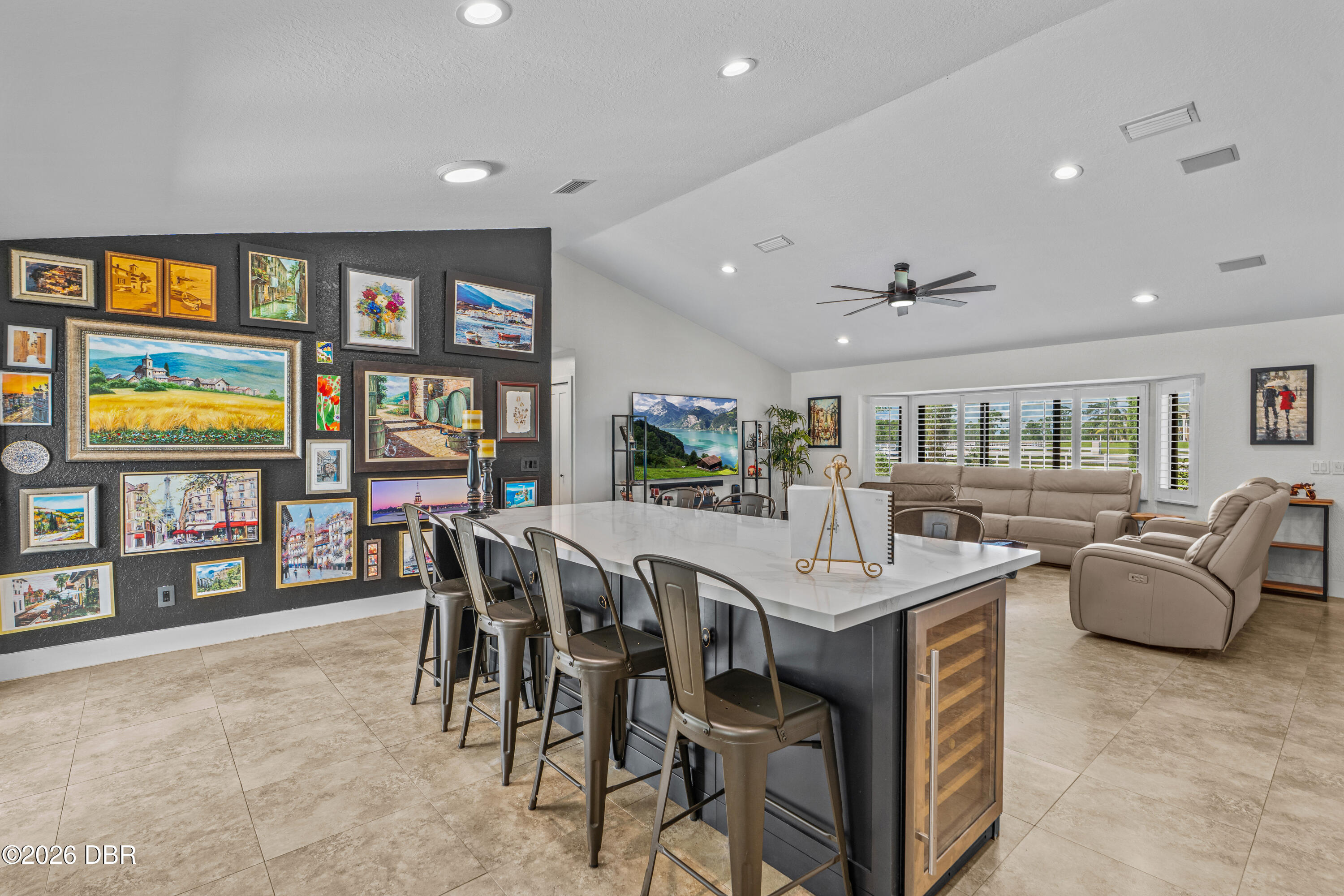 Open-plan kitchen with a large island and bar stools beside a gallery wall and beige living room seating.