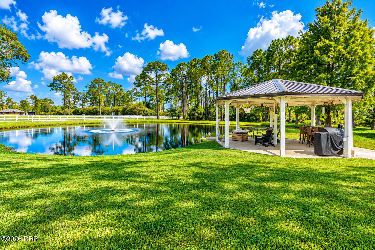 Backyard pond and fountain beside a covered pavilion with outdoor seating and a grill.