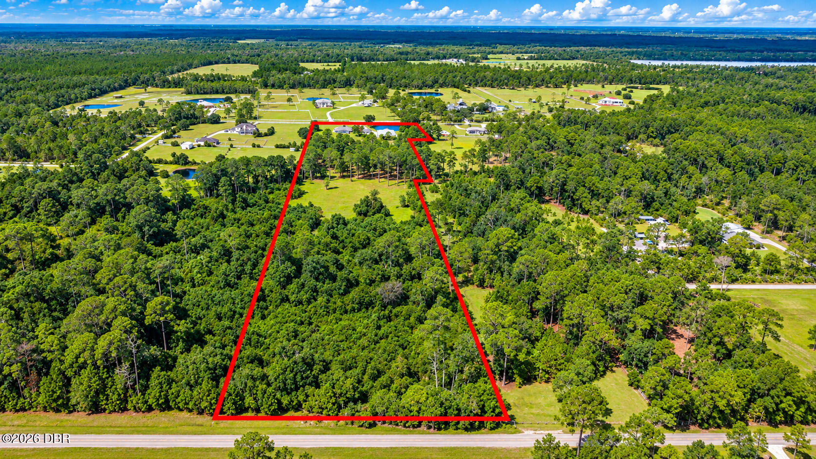 Aerial view of a wooded parcel outlined in red, with a grassy clearing and road frontage.