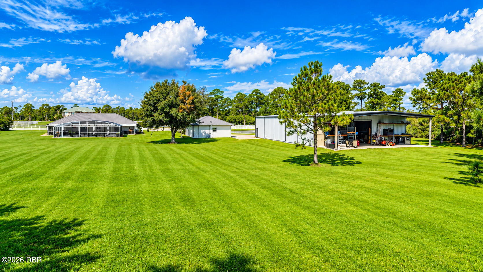 Broad green lawn with several detached buildings, a screened structure, and an open equipment shed.