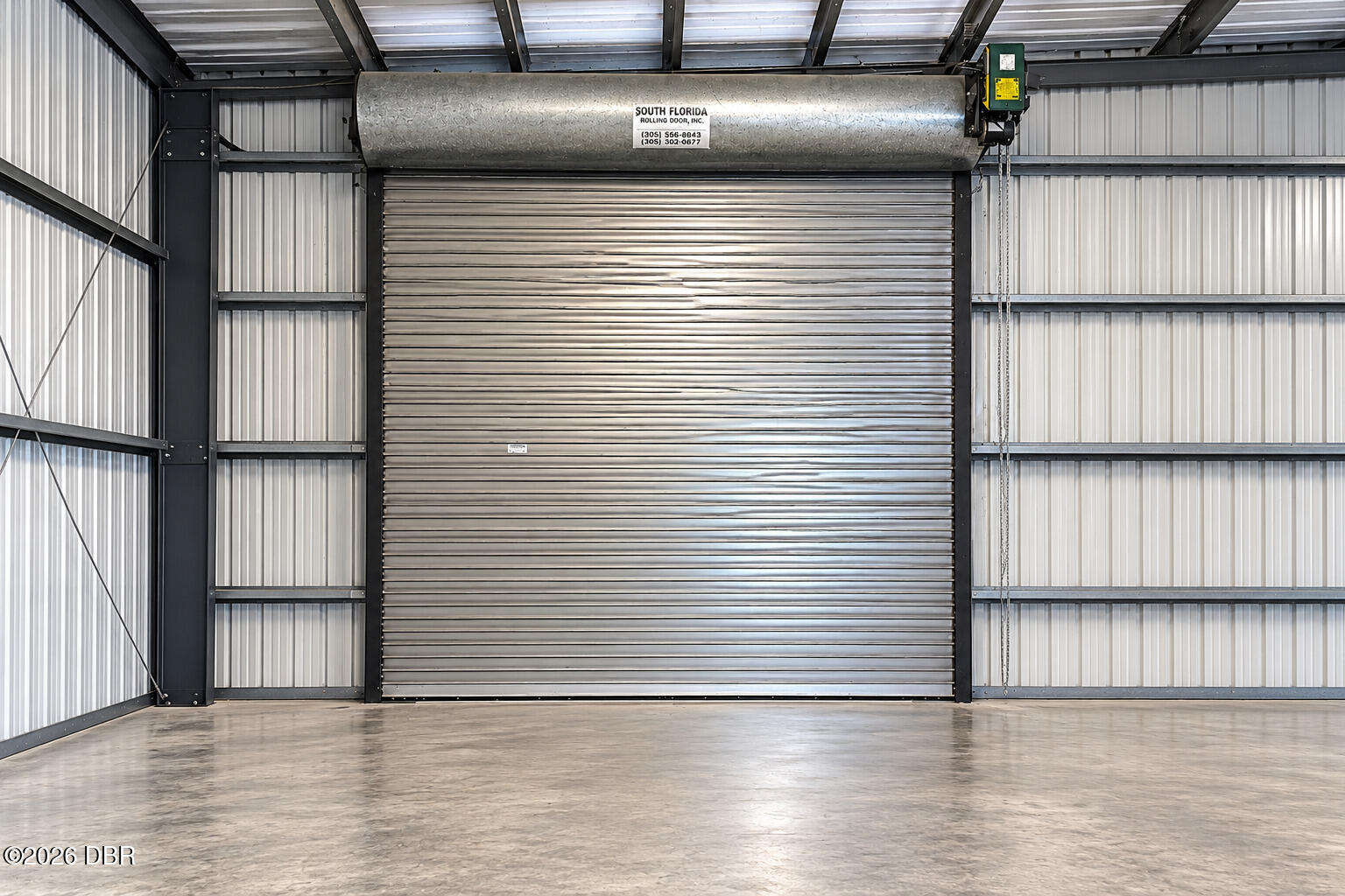Vacant metal garage interior with a large roll-up door and polished concrete floor.
