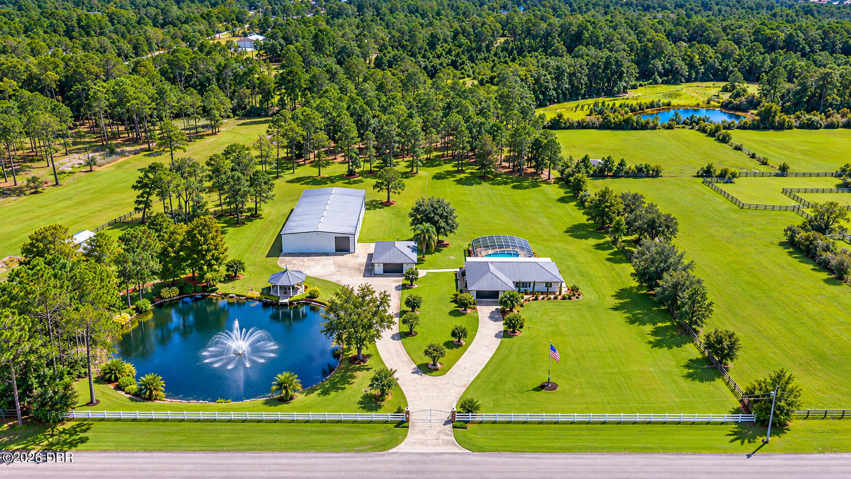 Aerial view of 4160 Saddle Club Drive with a fountain pond, screened pool, detached buildings, and broad lawns.