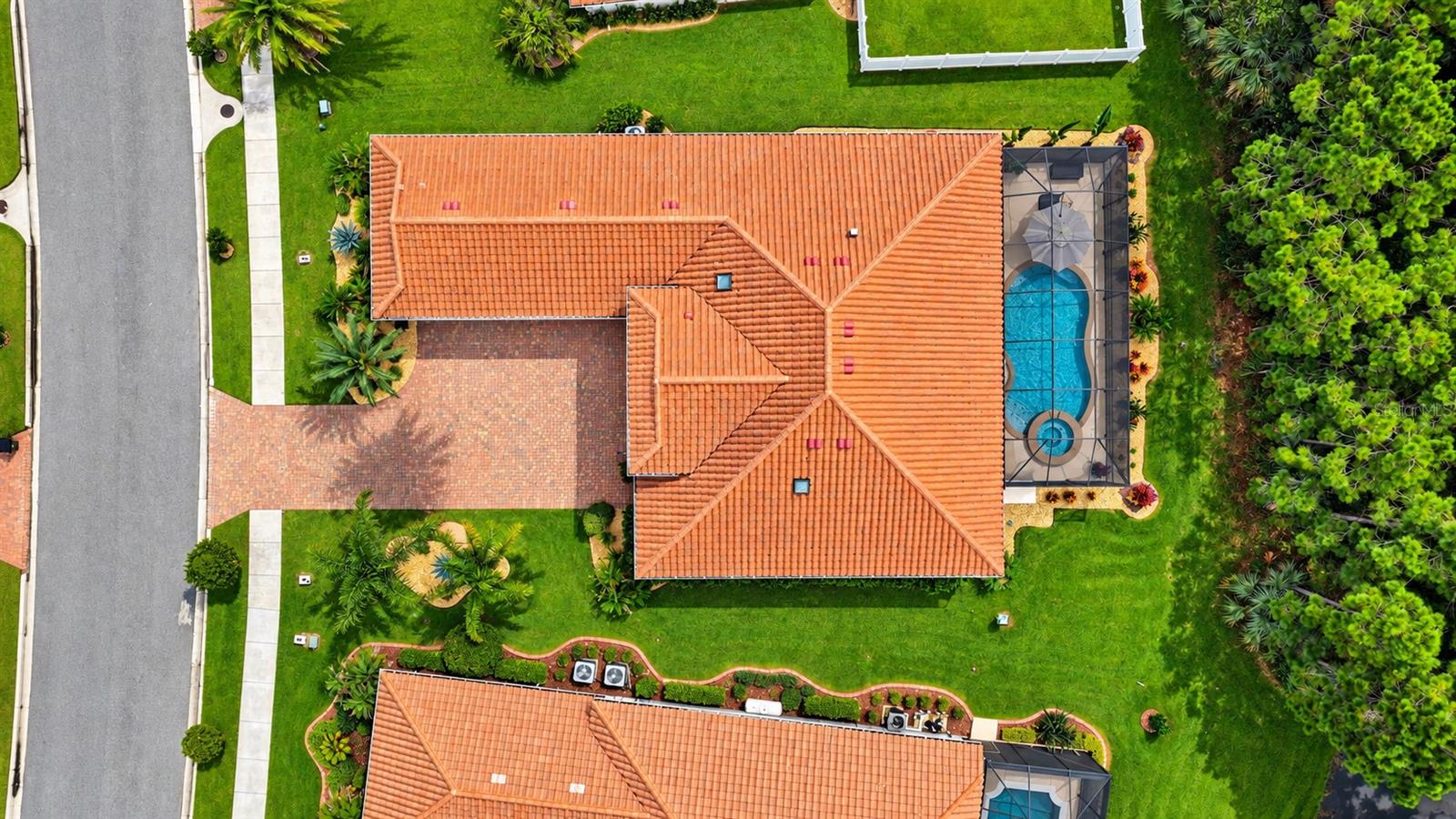 Aerial view of a tile-roofed home with a screened swimming pool and landscaped yard.