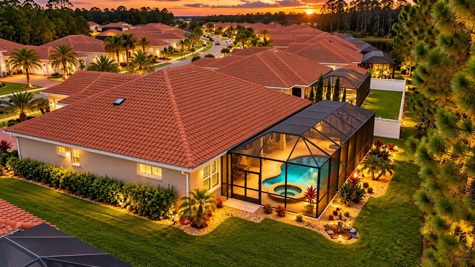 Aerial view of a tile-roofed home with a screened swimming pool at sunset.