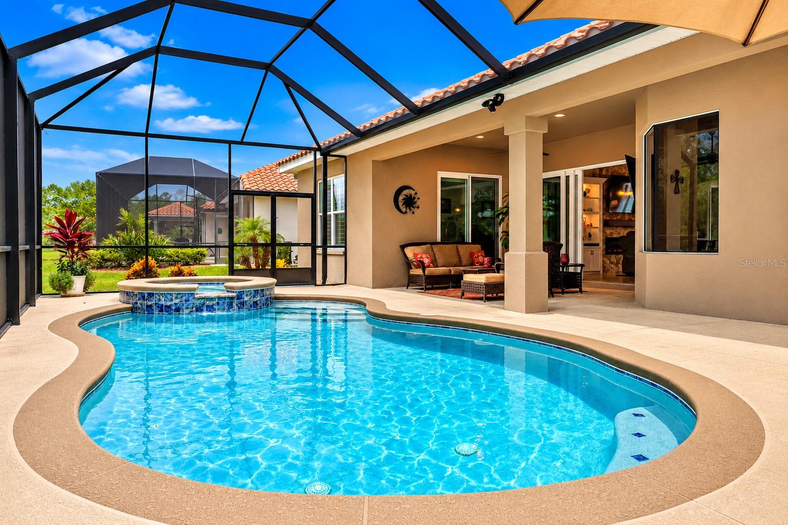 Curved pool and raised spa beneath a screened lanai beside a covered patio with outdoor seating.