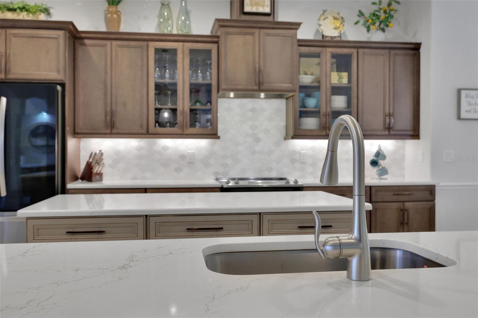 Kitchen with dark wood cabinets, patterned backsplash, and a large white island with an undermount sink.