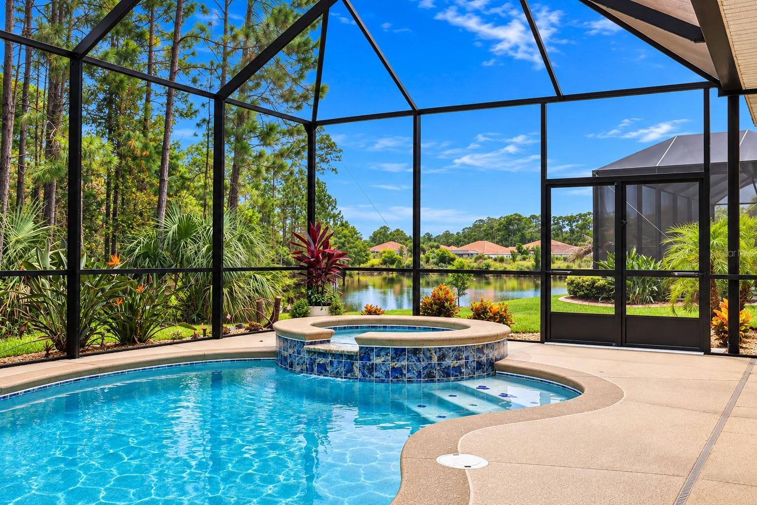 Screened backyard pool and raised spa overlooking a lake, surrounded by tropical landscaping.