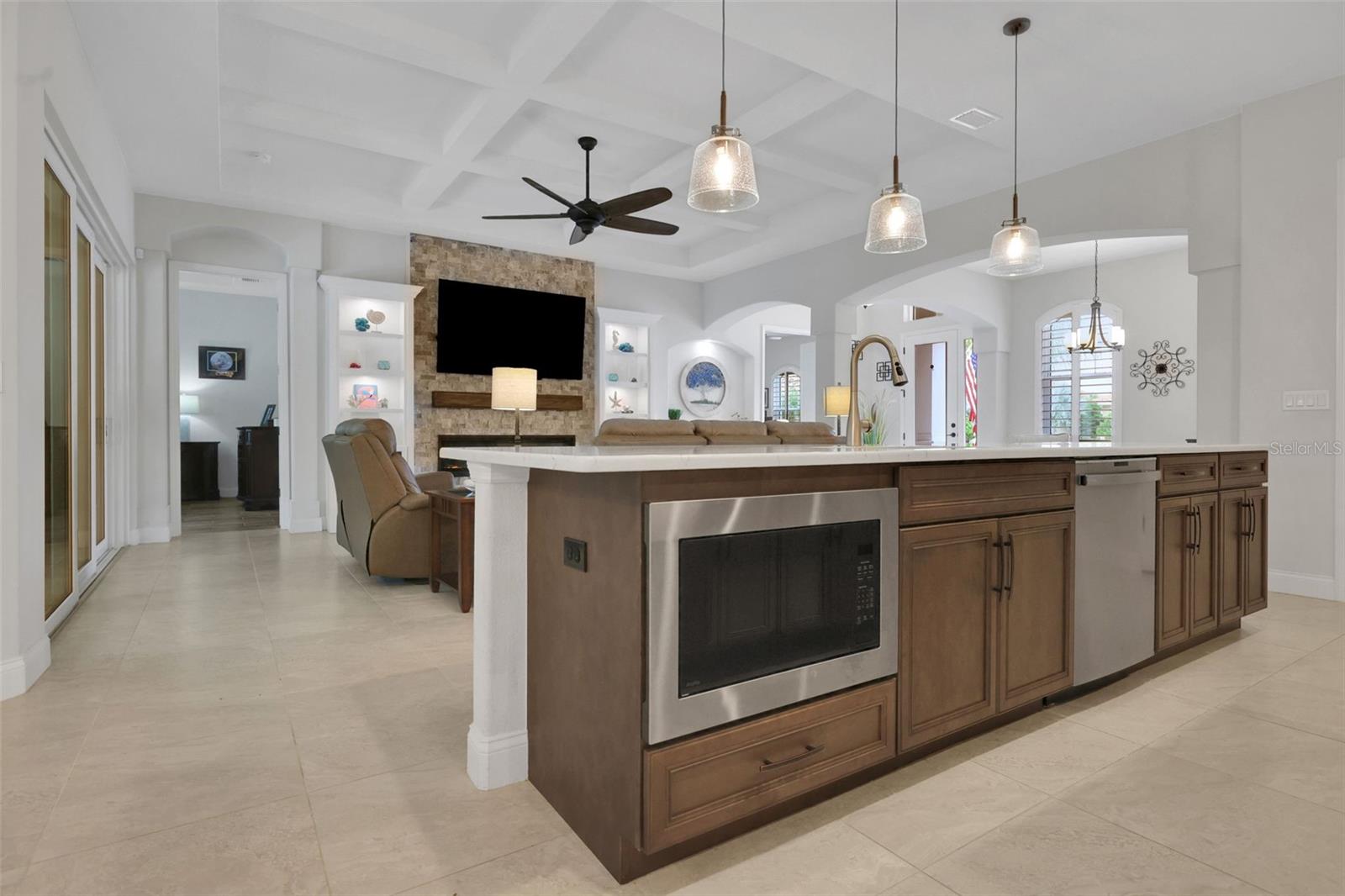 Open kitchen with a large wood island and built-in microwave, looking toward a living room with a stone fireplace.