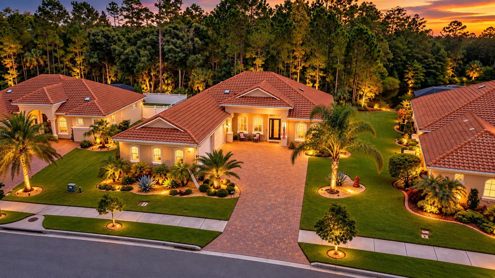 Aerial view of terracotta-roofed homes and palm-lined landscaping at sunset.