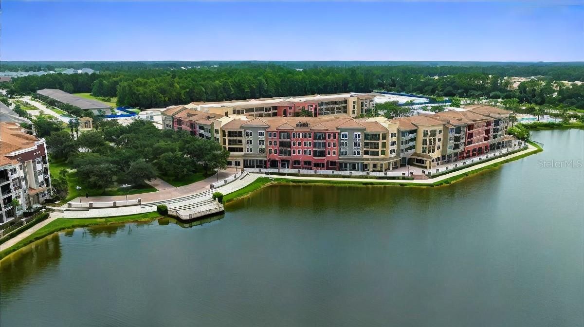 Waterfront condominium complex with landscaped paths and a lake, seen from above.