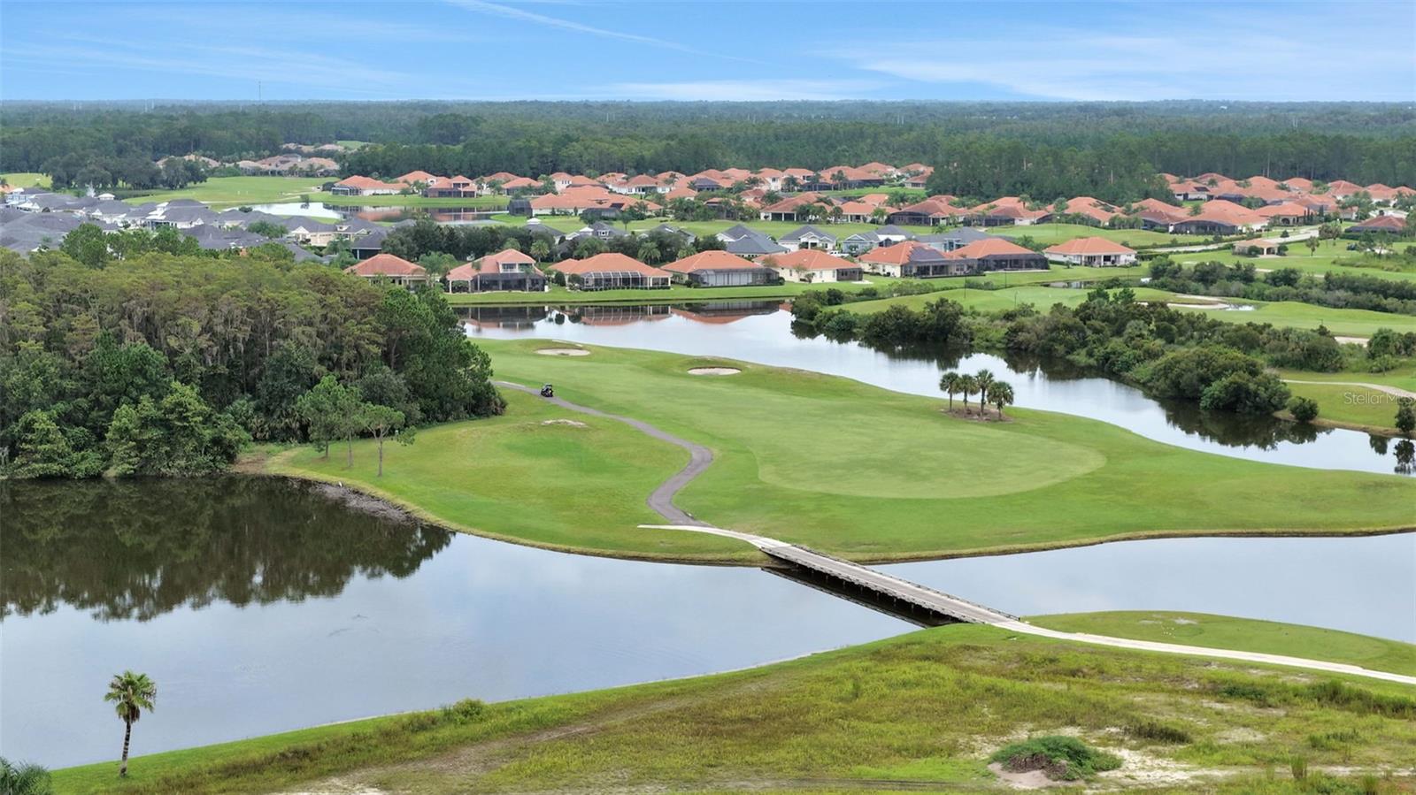 Aerial view of a golf course community with ponds, a footbridge, and terracotta-roofed homes.