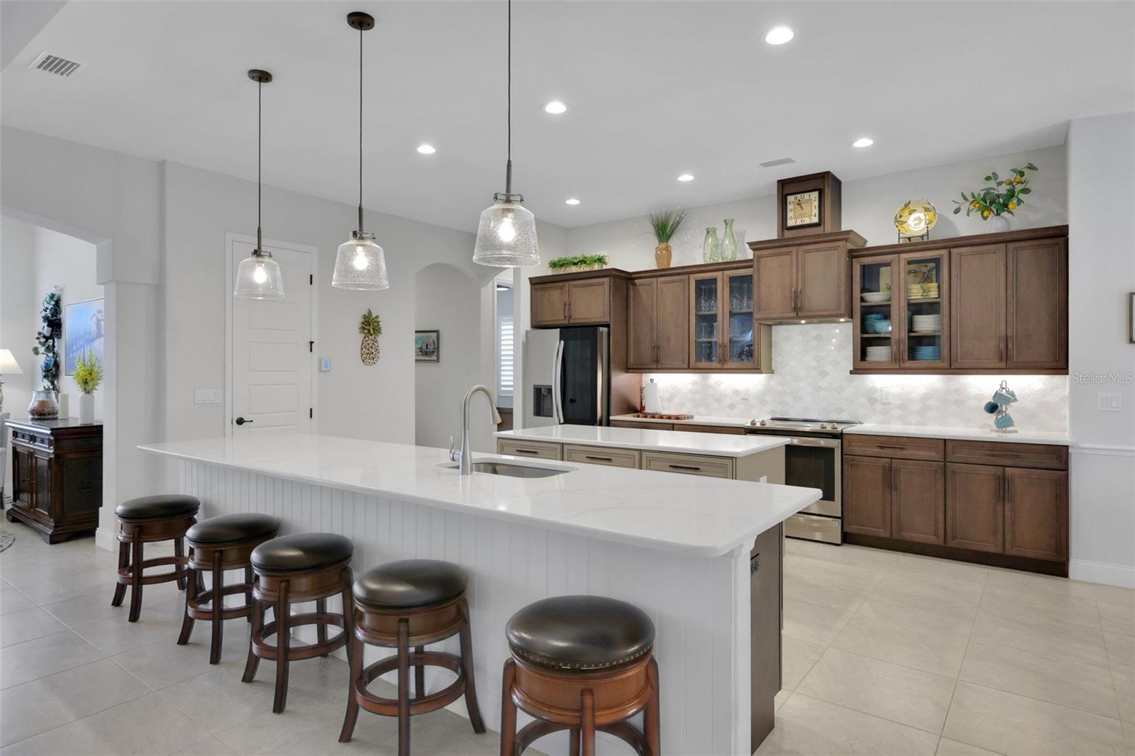 Kitchen with dark wood cabinets, stainless steel appliances, and a large island lined with bar stools.