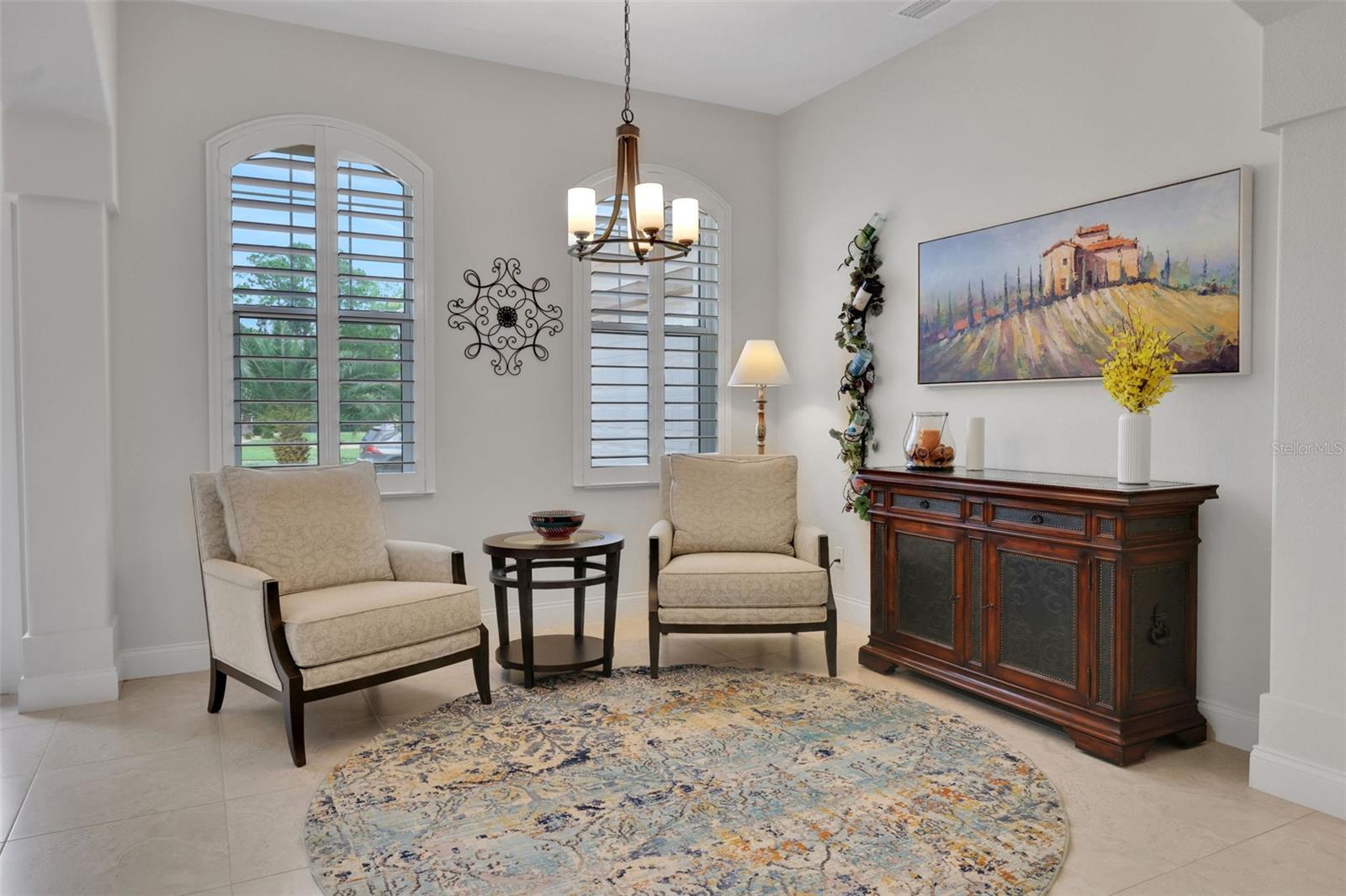 Sitting area with two armchairs, arched shuttered windows, and a dark wood sideboard.