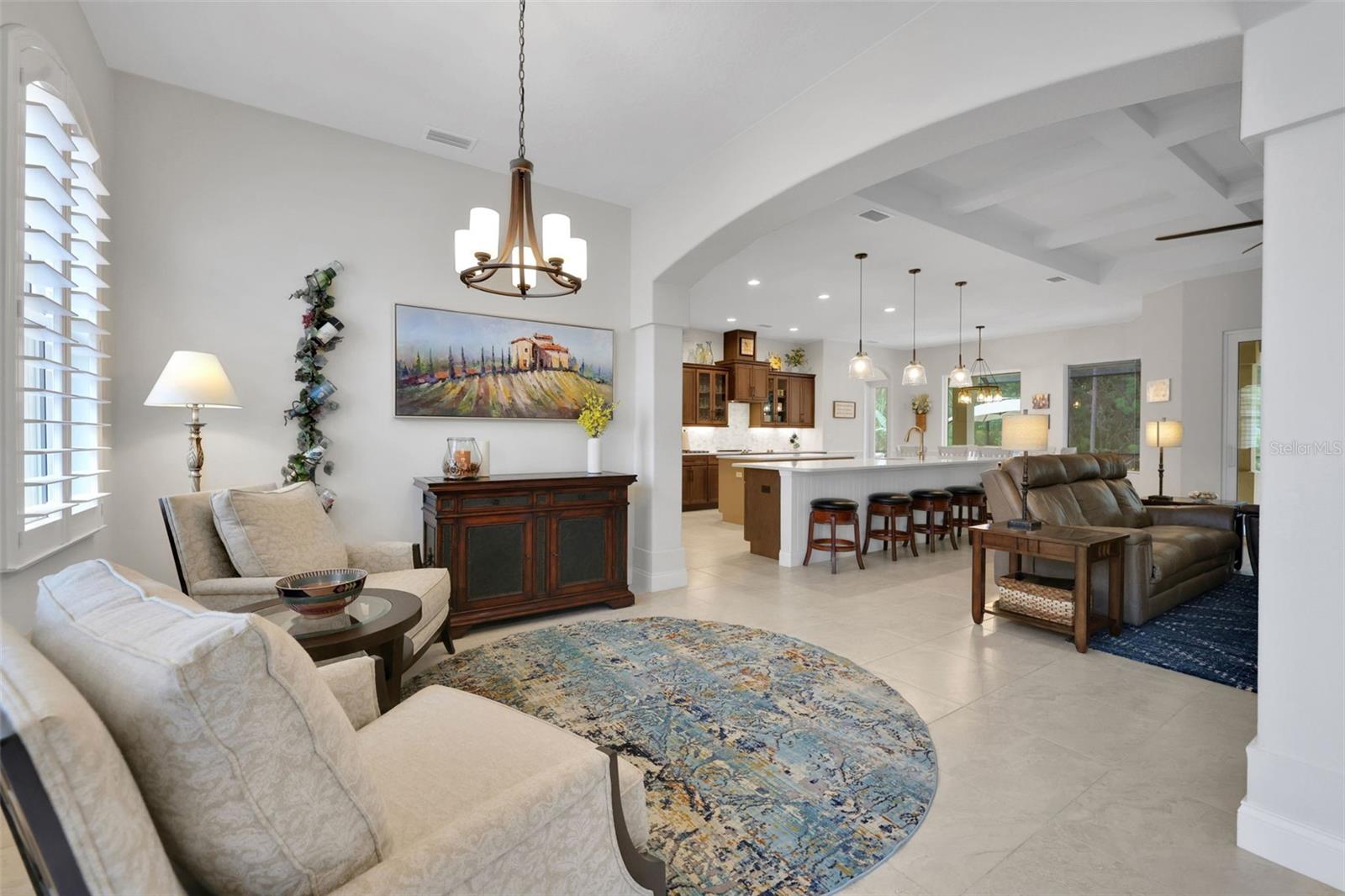 Open-plan living room with cream sofas, leather sectional, tiled floors, and kitchen island with bar stools.