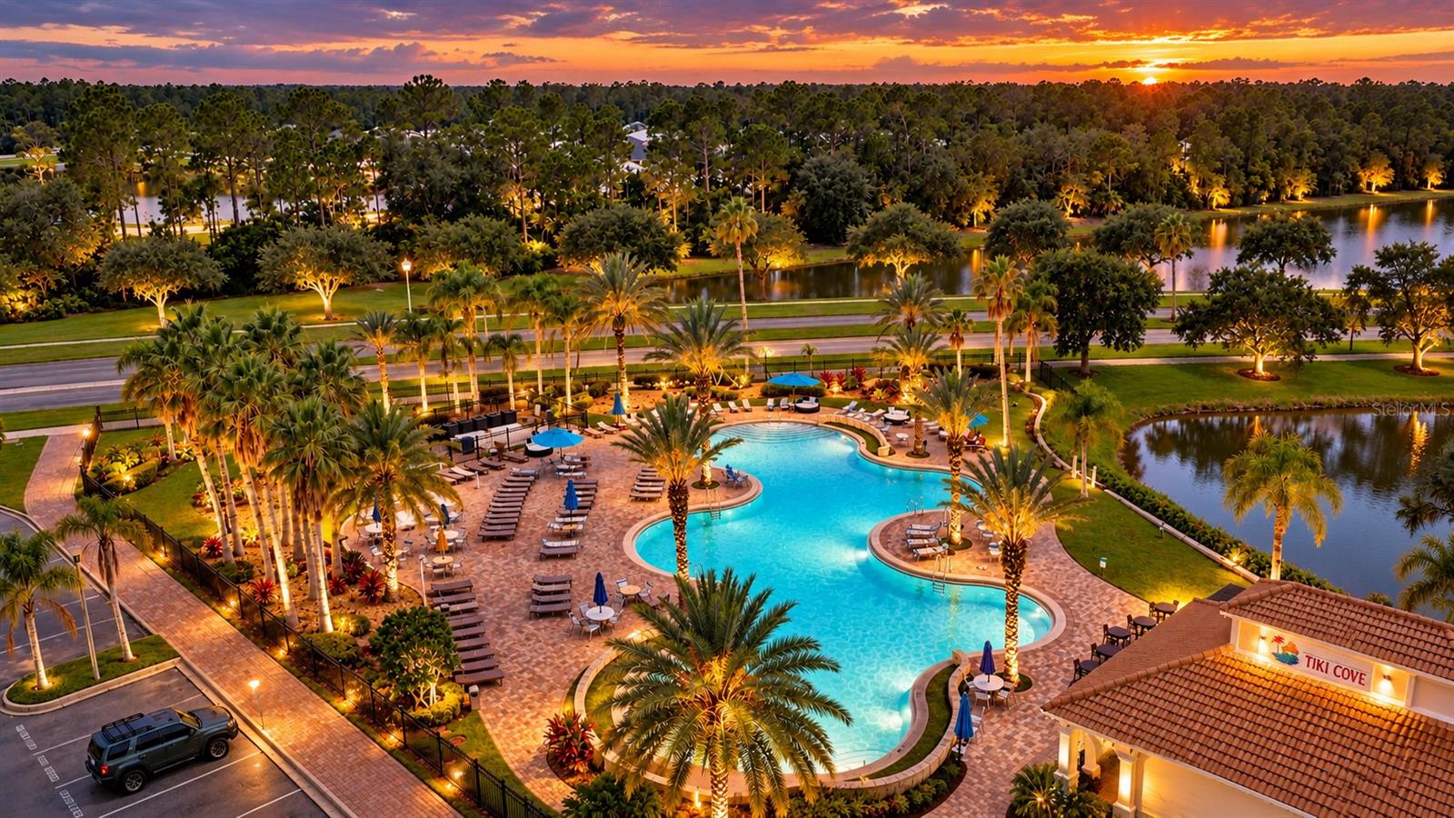 Aerial view of a resort-style pool with palm trees and lounge chairs at sunset.