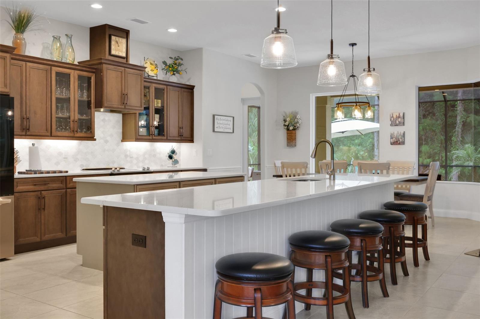 Kitchen with rich wood cabinets, a large white island, and a row of dark-cushioned bar stools.
