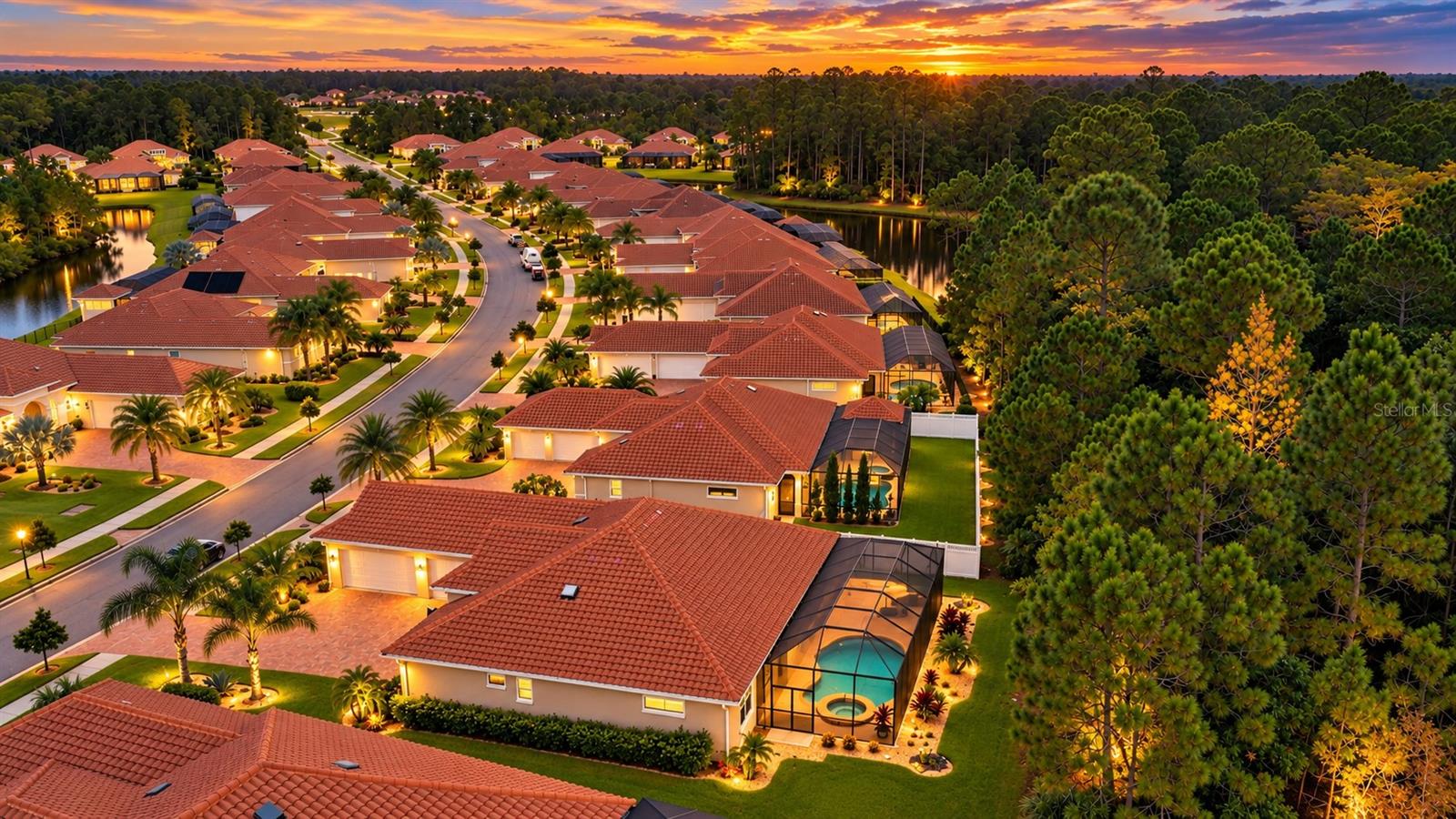 Aerial view of a tiled-roof home with a screened pool among lakeside homes at sunset.