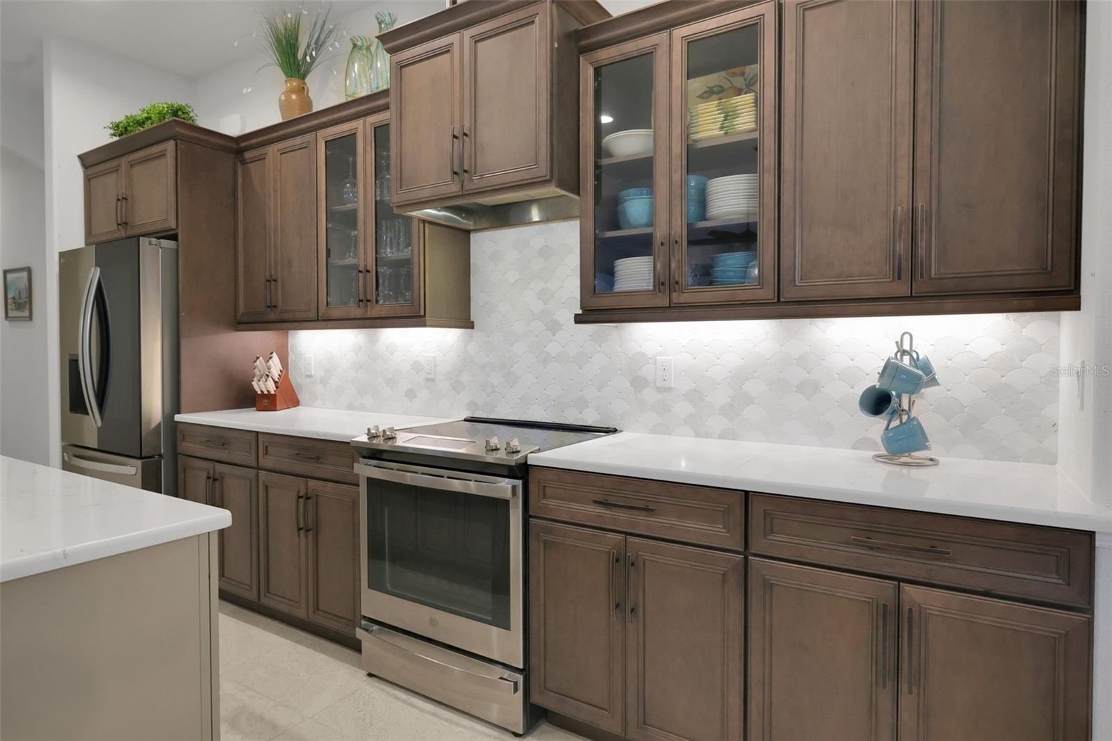 Kitchen with dark wood cabinets, white scalloped backsplash, and stainless steel appliances.