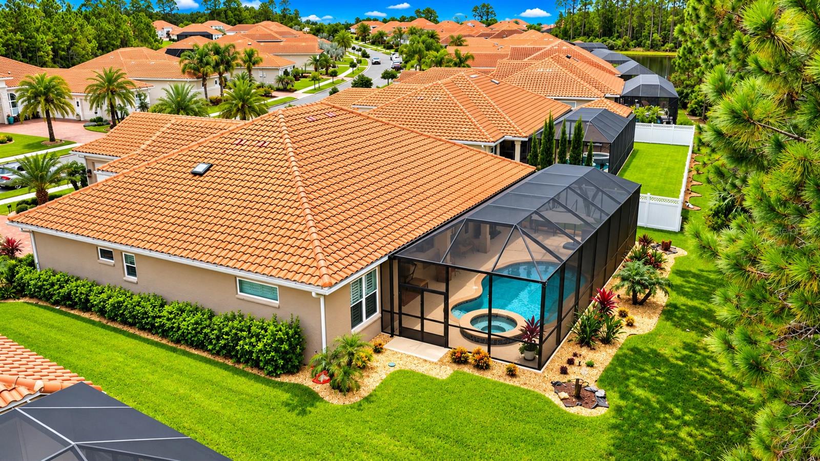 Aerial view of a tile-roofed home with a screened pool enclosure and landscaped yard.