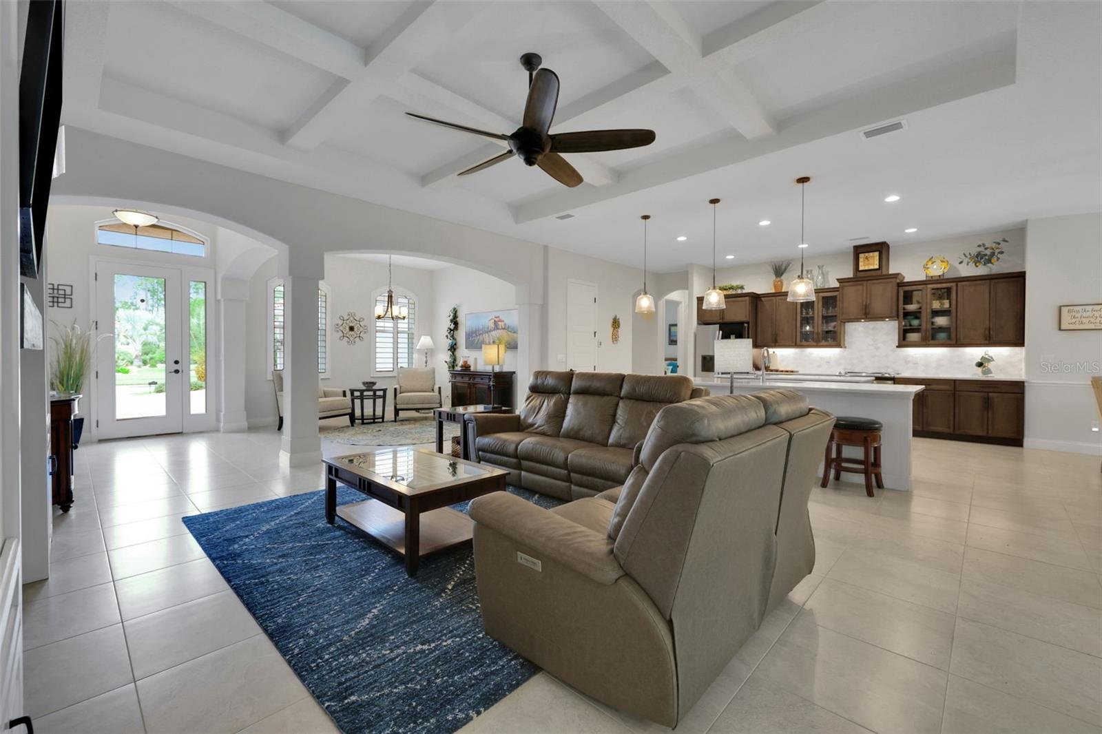 Open living room and kitchen with a coffered ceiling, dark wood cabinets, and a brown sectional.