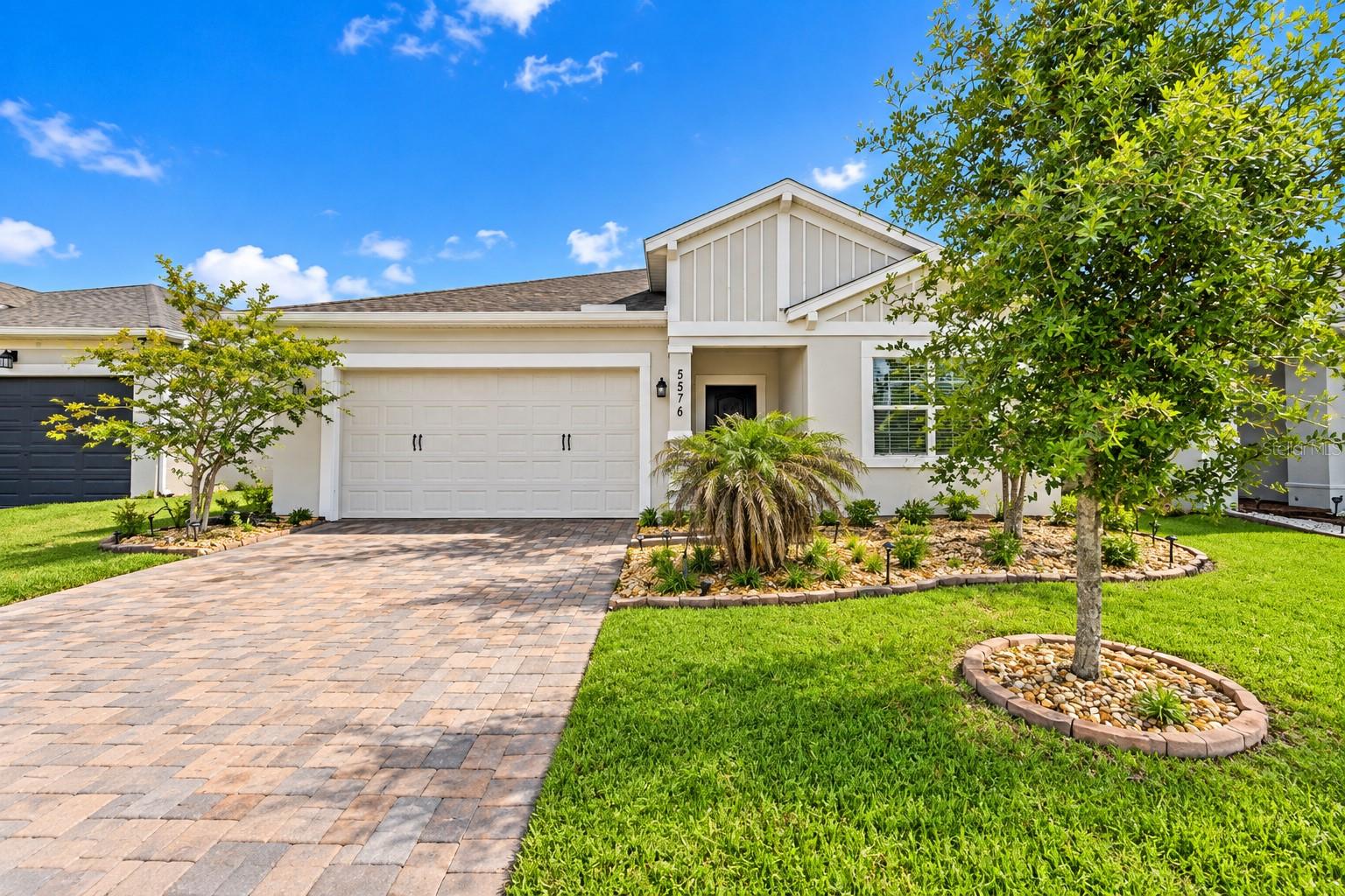Single-story home with a two-car garage, paver driveway, and landscaped front lawn.