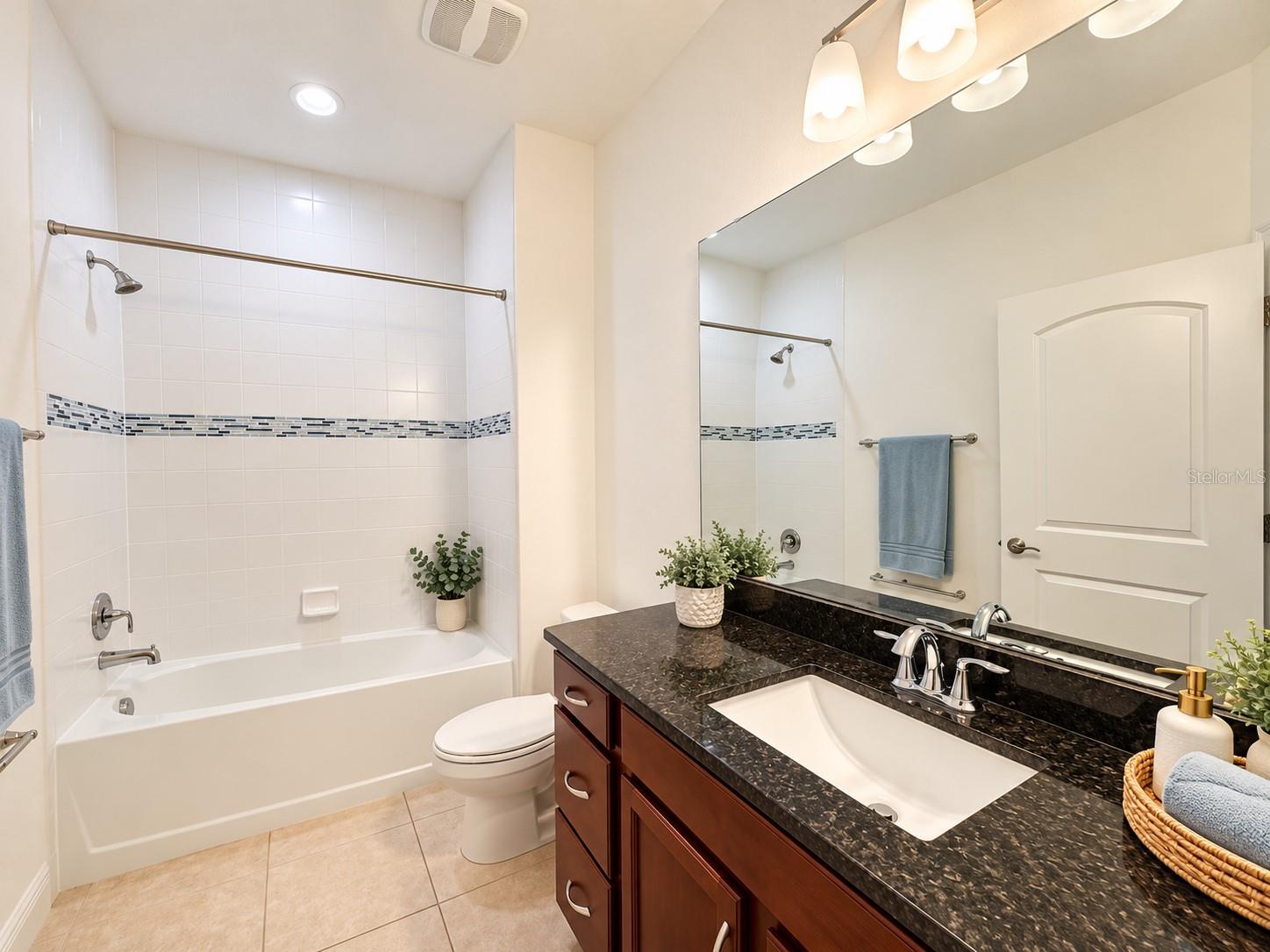 Bathroom with a tiled tub and shower, dark granite vanity, and large mirror.