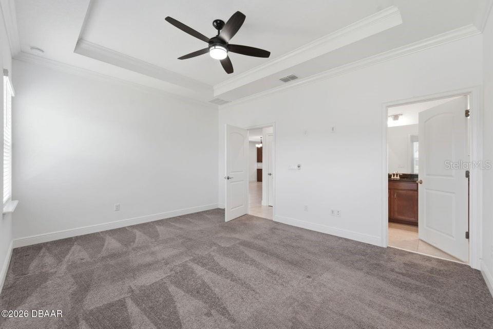 Empty bedroom with gray patterned carpet, tray ceiling, and dark ceiling fan.