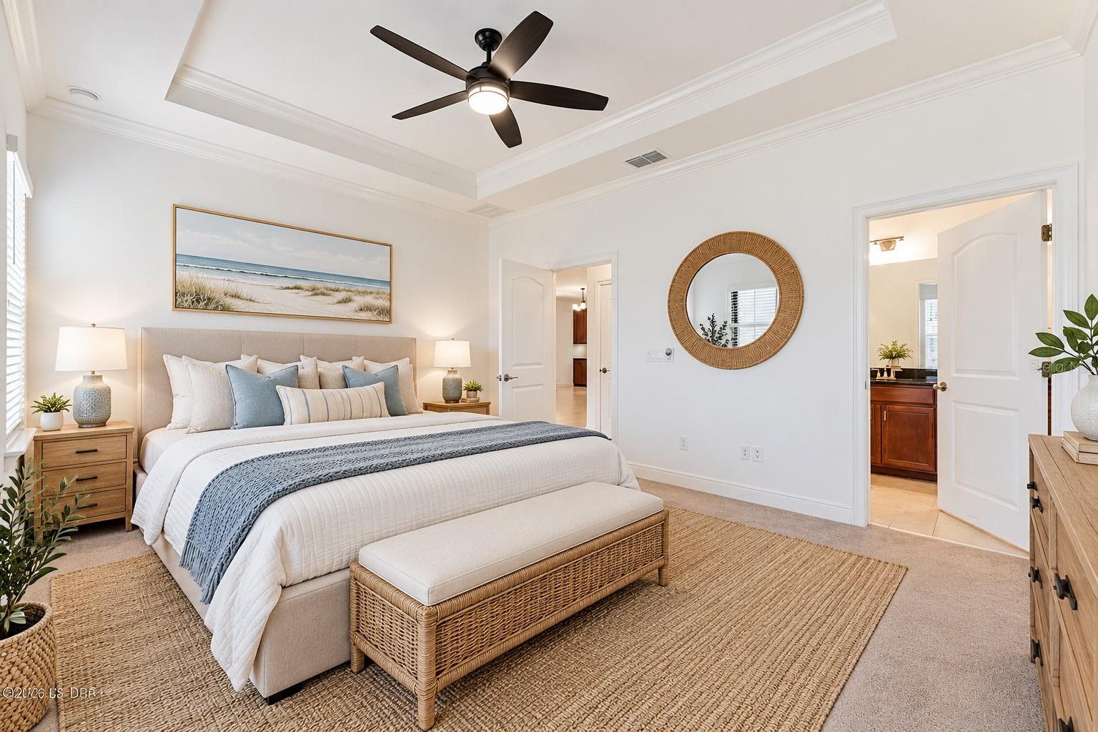 Staged bedroom with a king-size bed, tray ceiling, dark ceiling fan, and coastal artwork.