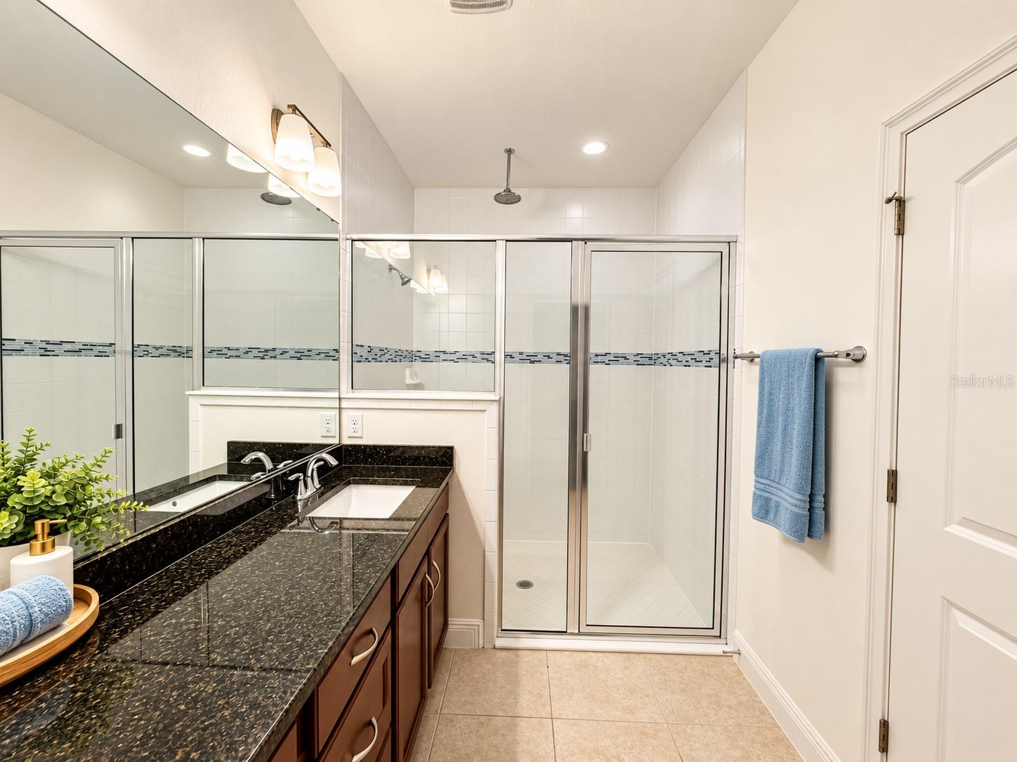 Bathroom with a dark granite double vanity and a glass-enclosed shower.