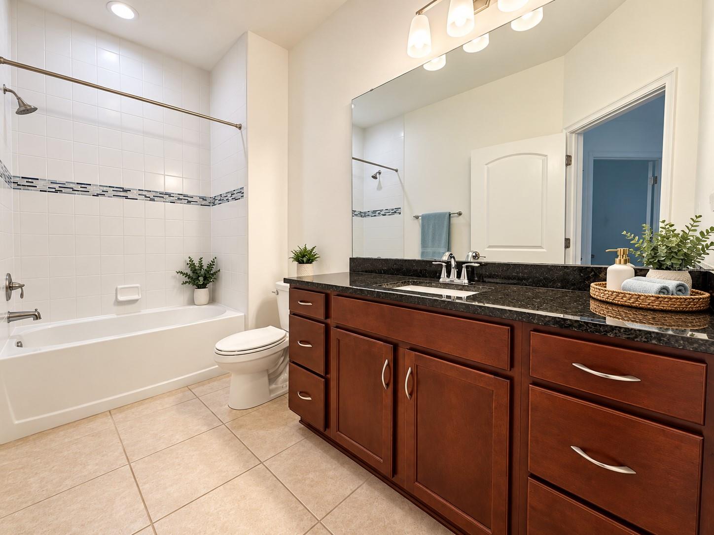 Bathroom with tiled tub and shower beside a cherry wood vanity with dark stone countertop.