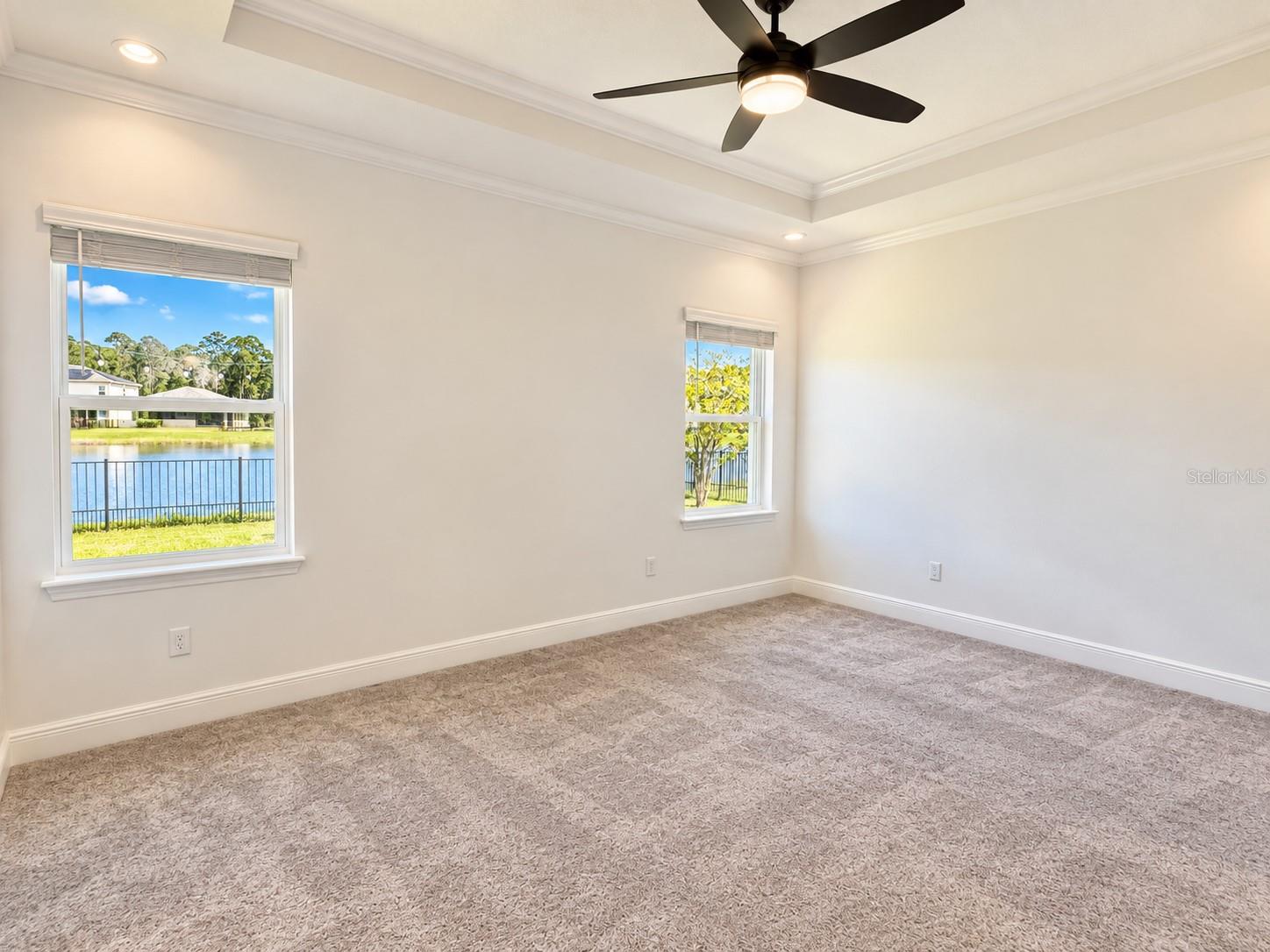Empty carpeted room with a ceiling fan and windows overlooking a pond.