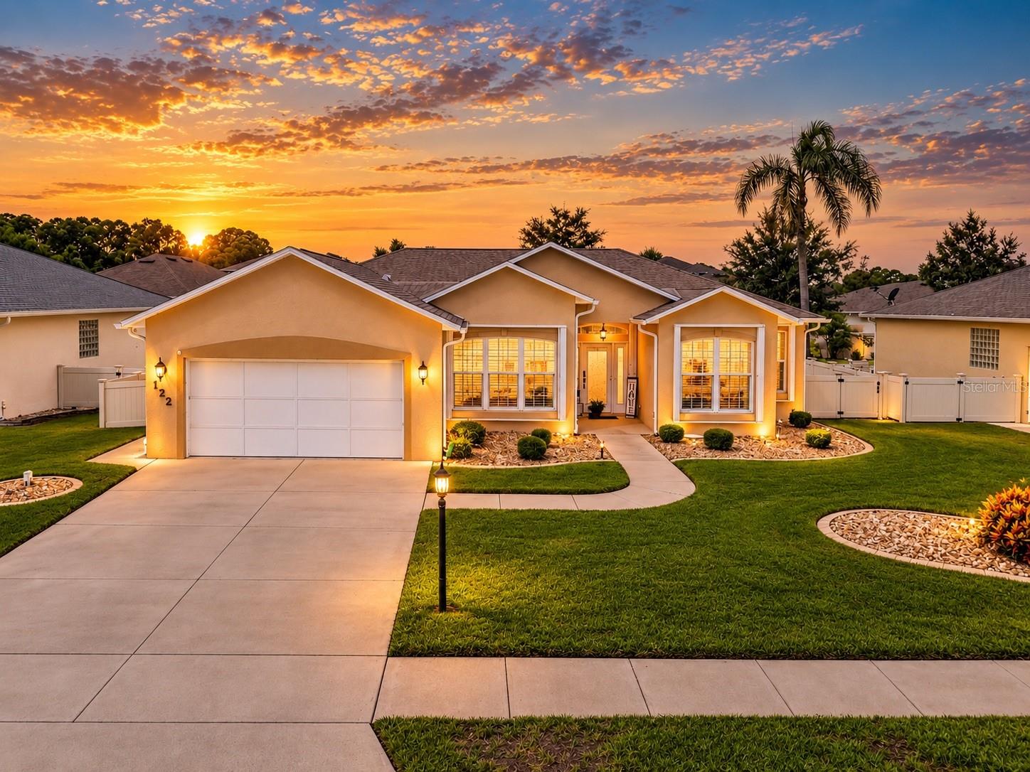 Single-story home with a two-car garage and landscaped lawn beneath a colorful sunset.
