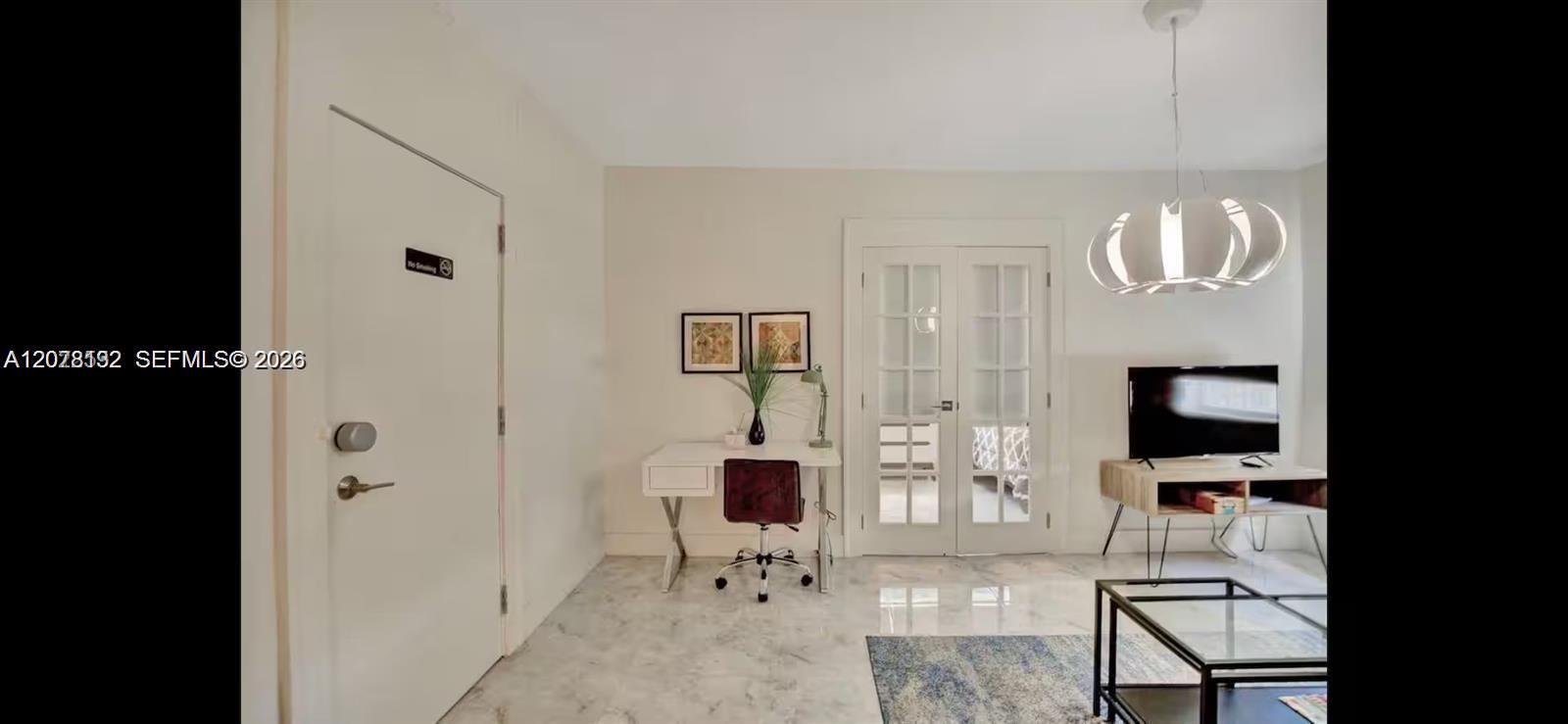 Furnished living room with a desk, glass-paneled double doors, and a television.