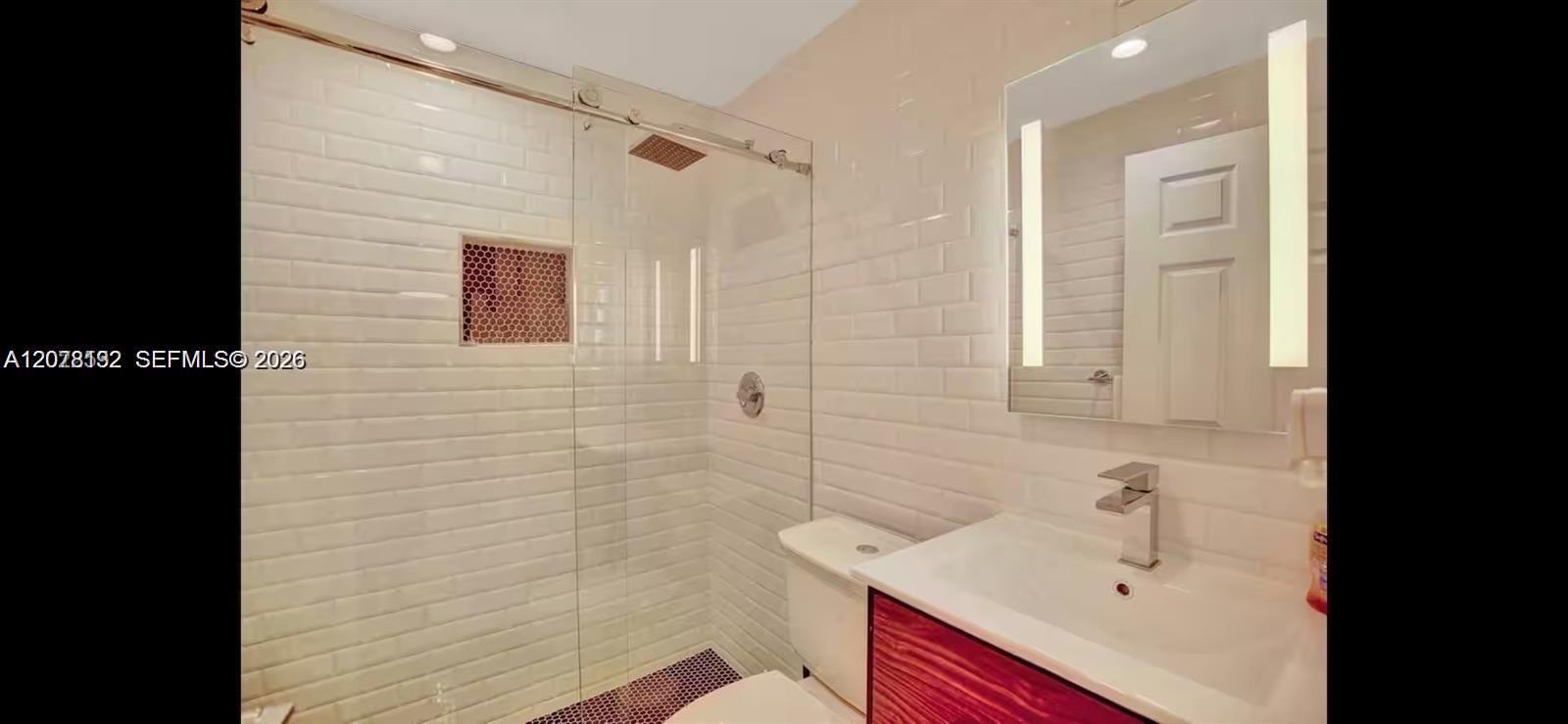 Bathroom with a glass shower, white subway tile, and a wood-front vanity.