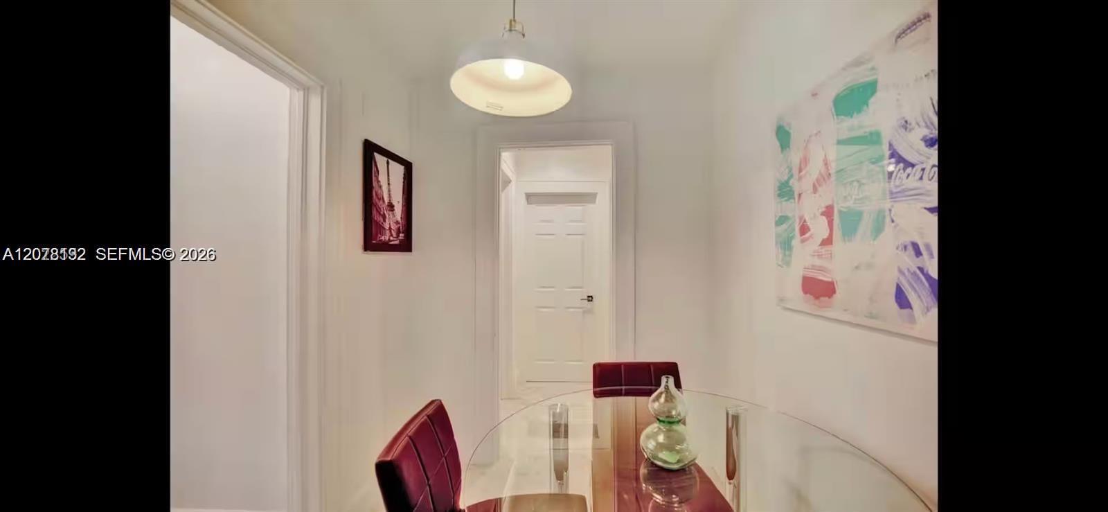 Dining room with a glass-top table, deep red chairs, and colorful abstract wall art.