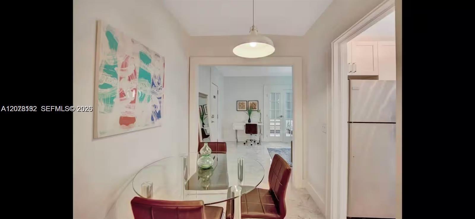 Dining area with a round glass table and burgundy chairs, opening into a bright office and living space.