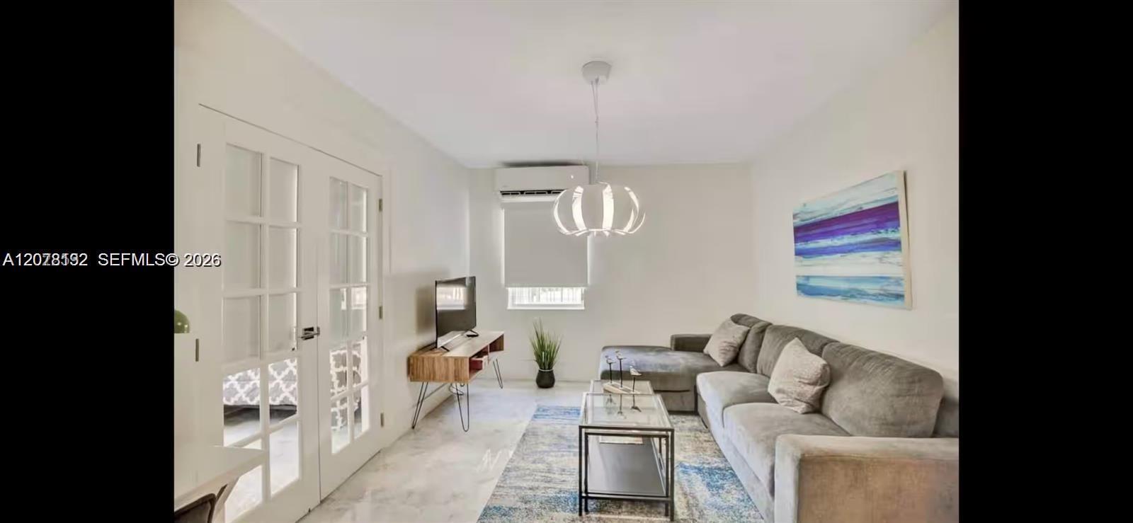 Living room with a gray sectional, glass coffee table, blue-toned rug, and French doors.
