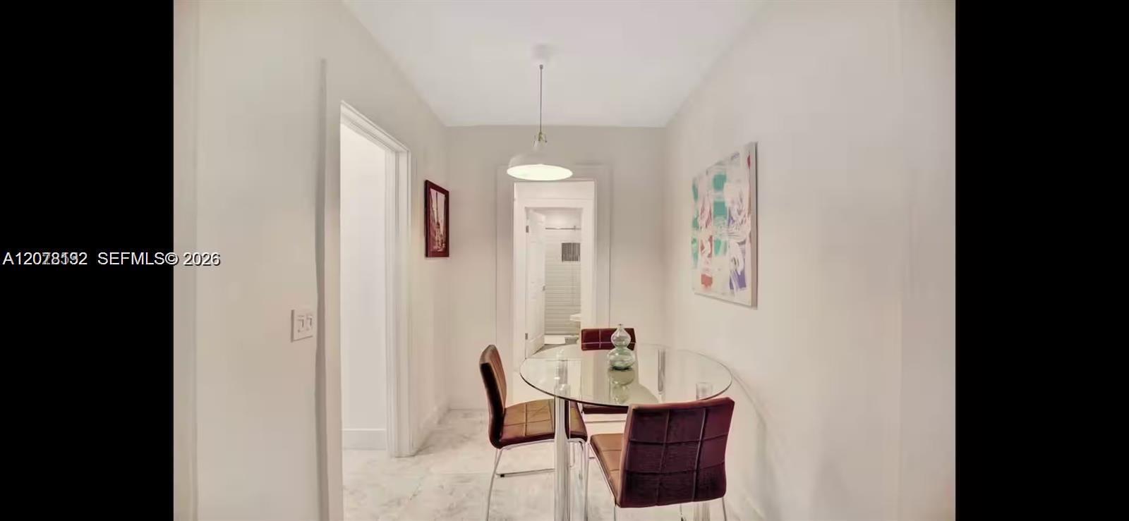 Dining area with a glass table, burgundy chairs, pendant light, and colorful wall art.