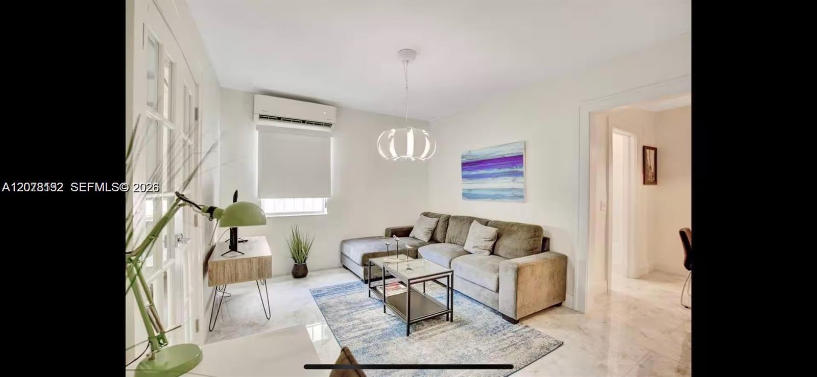 Living room with a gray sectional, glass coffee table, blue-gray rug, and desk beside tall windows.