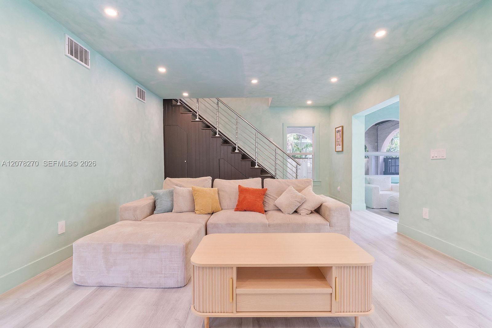 Furnished living room with a pale sectional sofa, light wood coffee table, and staircase with metal railing.