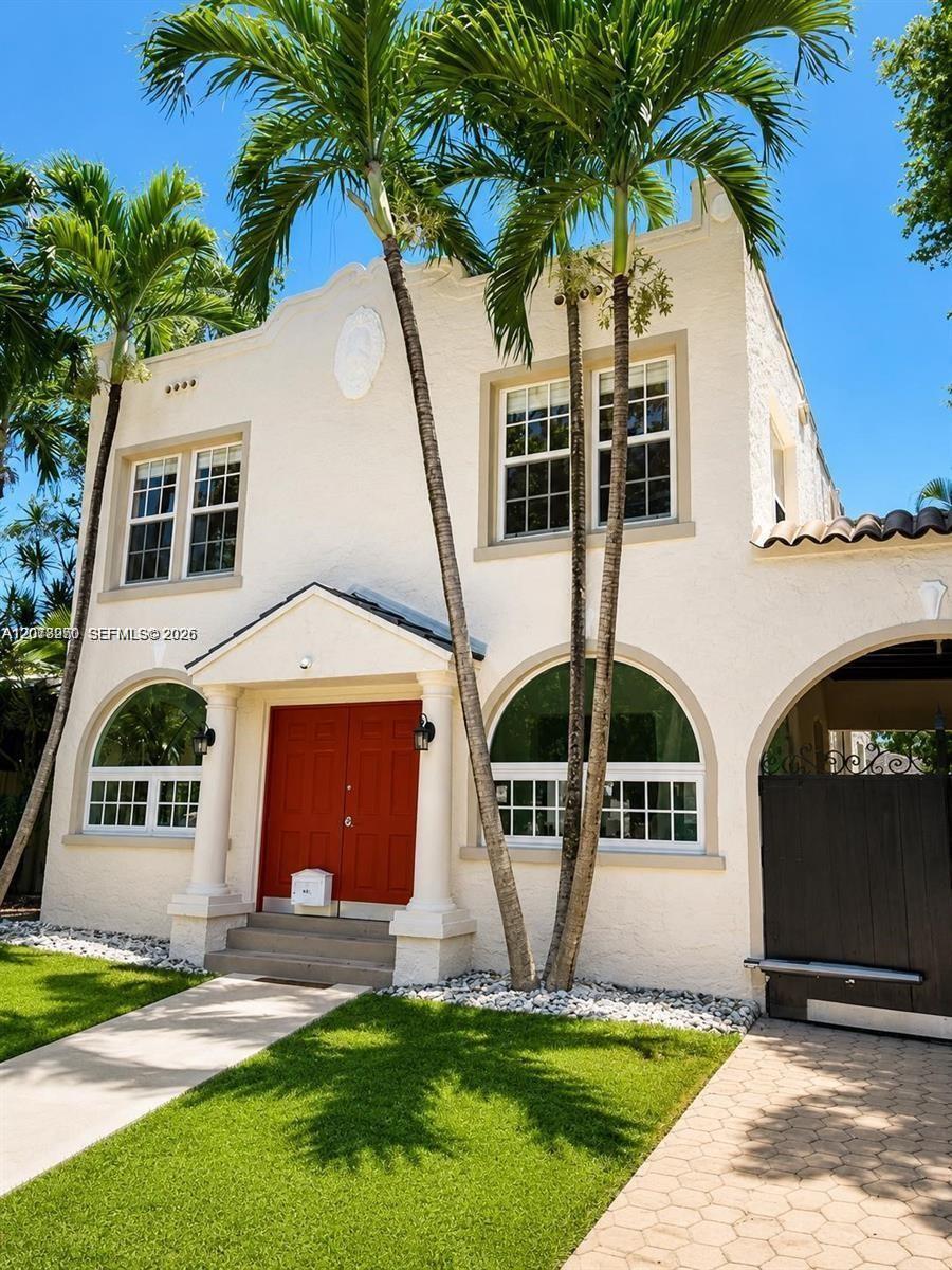 Cream stucco home with a red front door, arched windows, and tall palms.