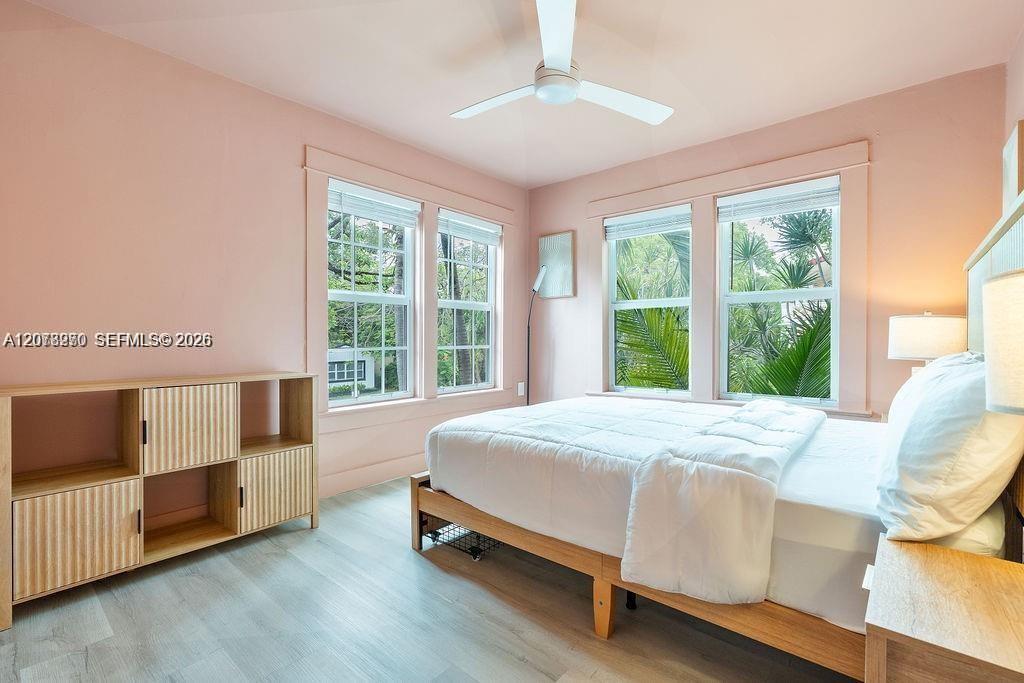 Bedroom with blush-pink walls, a white bed, and large windows overlooking tropical greenery.