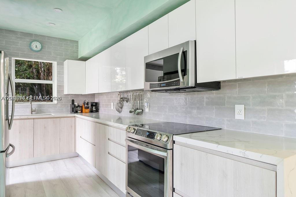 Modern kitchen with white cabinets, gray tile backsplash, and stainless steel appliances.