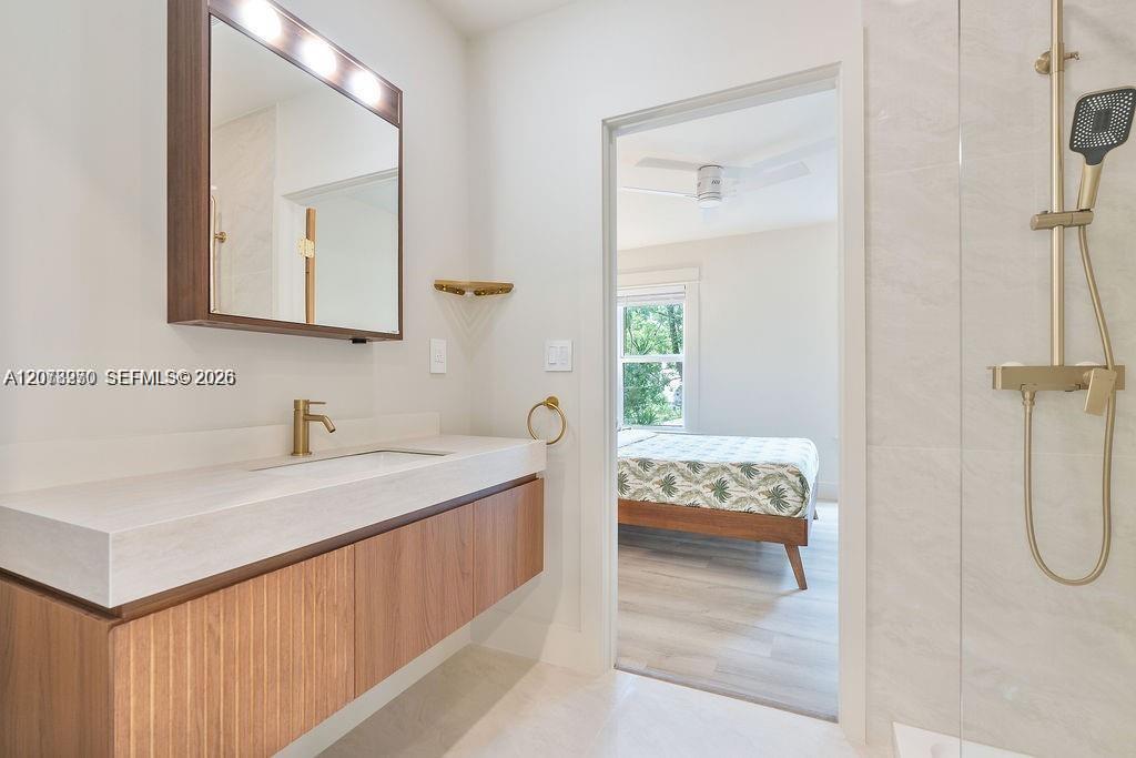 Modern bathroom with a floating wood vanity and gold fixtures, opening into a bedroom.