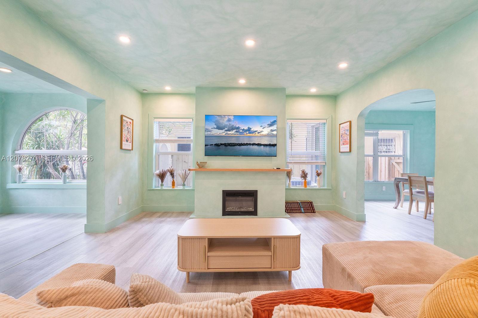 Furnished living room with a central fireplace, mint walls, arched openings, and neutral seating with an orange cushion.