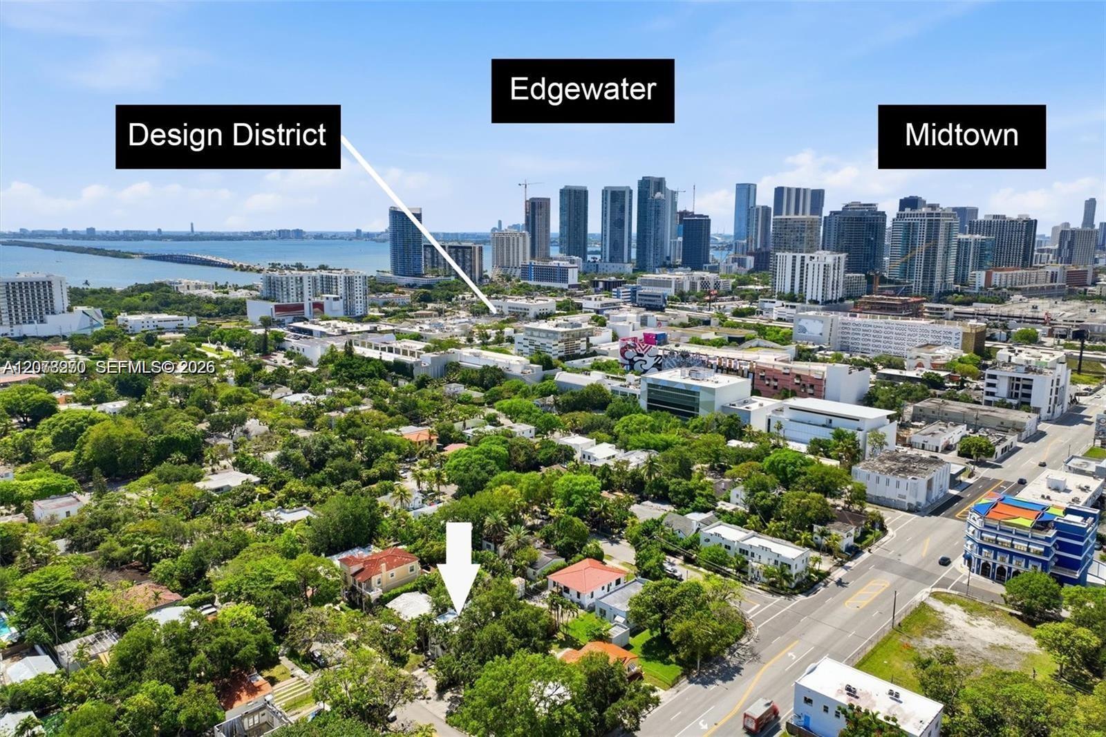 Aerial view of a leafy Miami neighborhood, with an arrow marking a property and the skyline beyond.