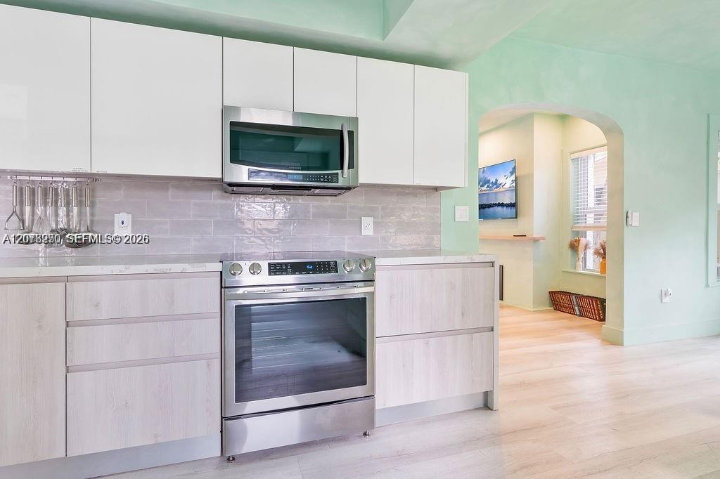 Modern kitchen with pale wood cabinets, stainless steel appliances, and a gray tile backsplash.