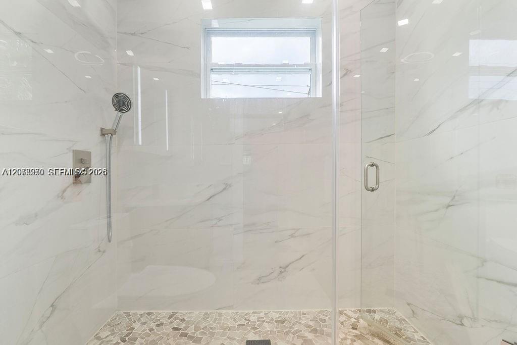 Walk-in shower with marble-look walls, clear glass enclosure, handheld showerhead, and mosaic tile floor.
