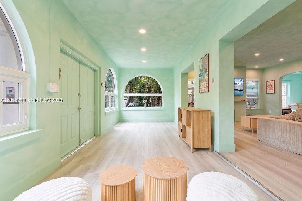 Foyer with mint-green walls, arched windows, pale wood floors, and a matching front door.
